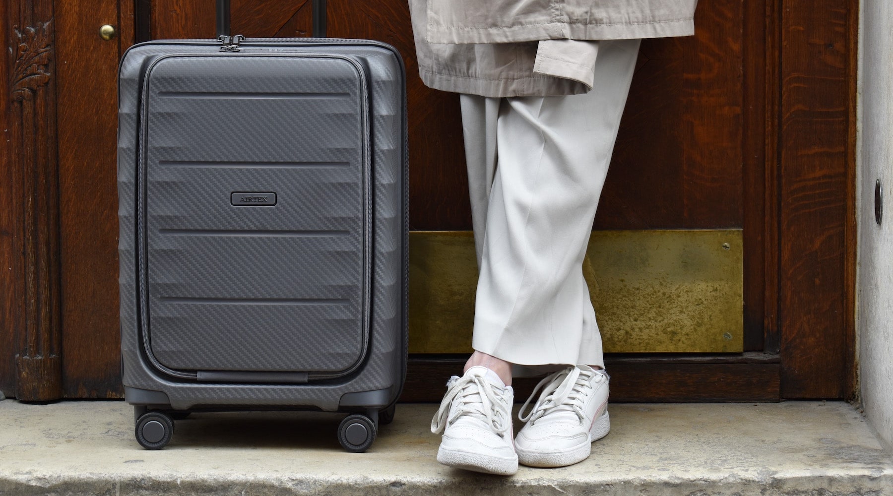 Valise cabine Airtex en carbone anthracite, posée devant une porte en bois sculpté